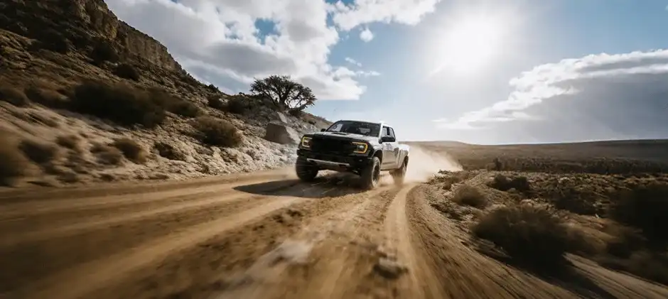 A white pickup truck using 4 High to drive at speed on a wide, dusty gravel road, demonstrating traction and control on a loose surface.