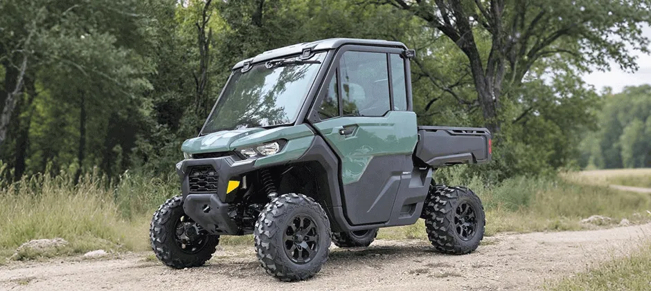 A dark green Can-Am Defender HD9 utility side-by-side on a narrow path surrounded by lush green trees.