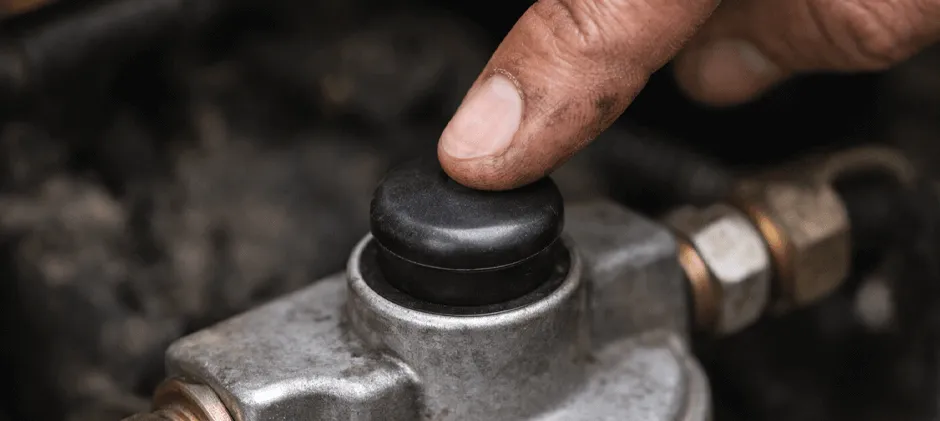 A mechanic's finger pressing the manual hand primer button on a diesel fuel filter head.