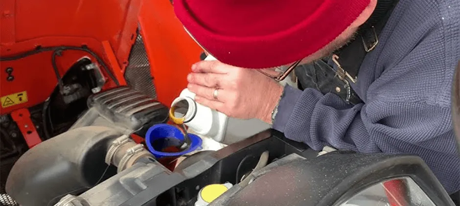 A-person-is-adding hydraulic-fluid-to-the-oil-filler-hole-on-the-hydraulic-tank-of-a-Kubota-Tractor